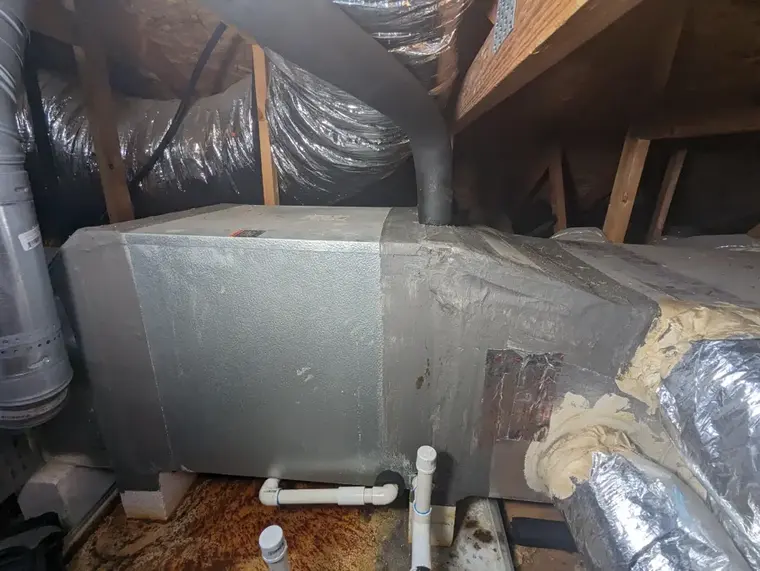 Attic air handler with a rusted condensate pan above a Flower Mound ceiling